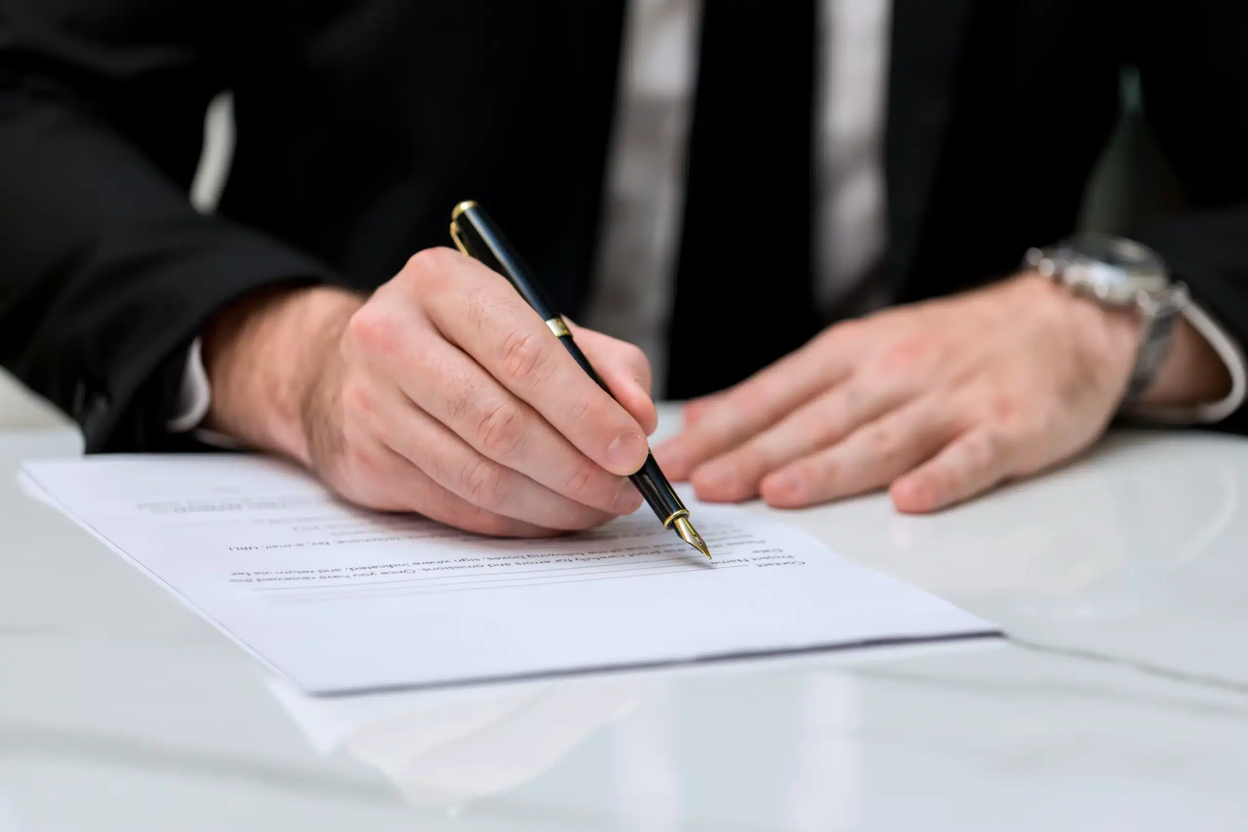 Person in a business suit signing a non-compete agreement with a black pen.