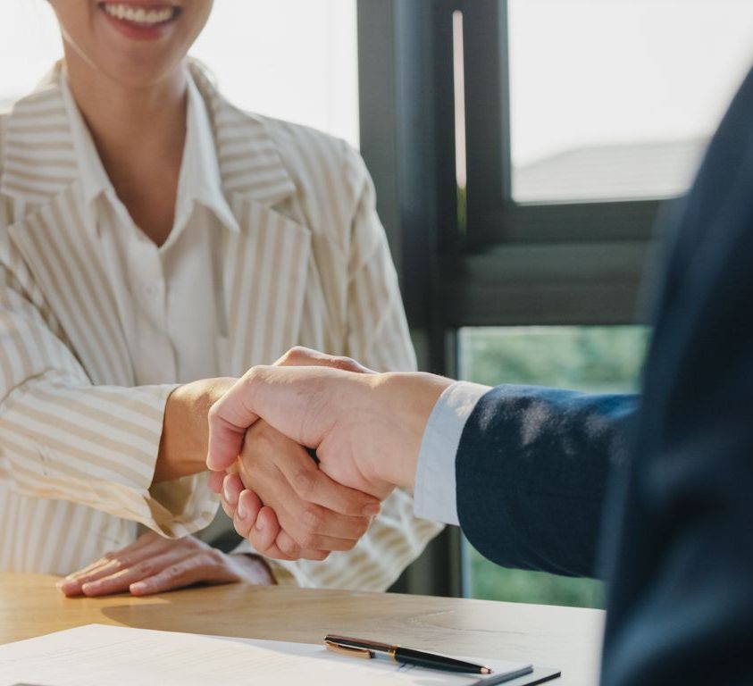Closeup of young Asian businessman sign a contract investment professional document agreement and shake hands at office. Businesspeople in workplace.