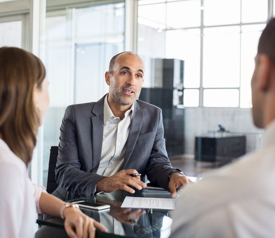 Mature financial agent showing new investment to young couple. Happy financial advisor discussing with a couple their mortgage loan. Happy couple consulting their bank agent about savings plan.