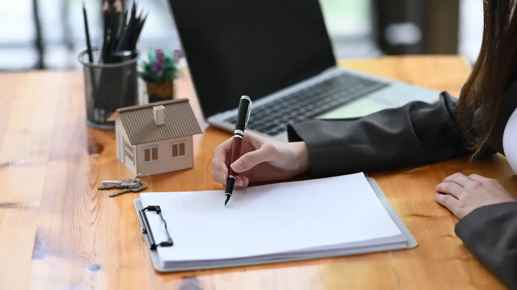 Property dispute attorney writing on a document with miniature house and laptop on the desk